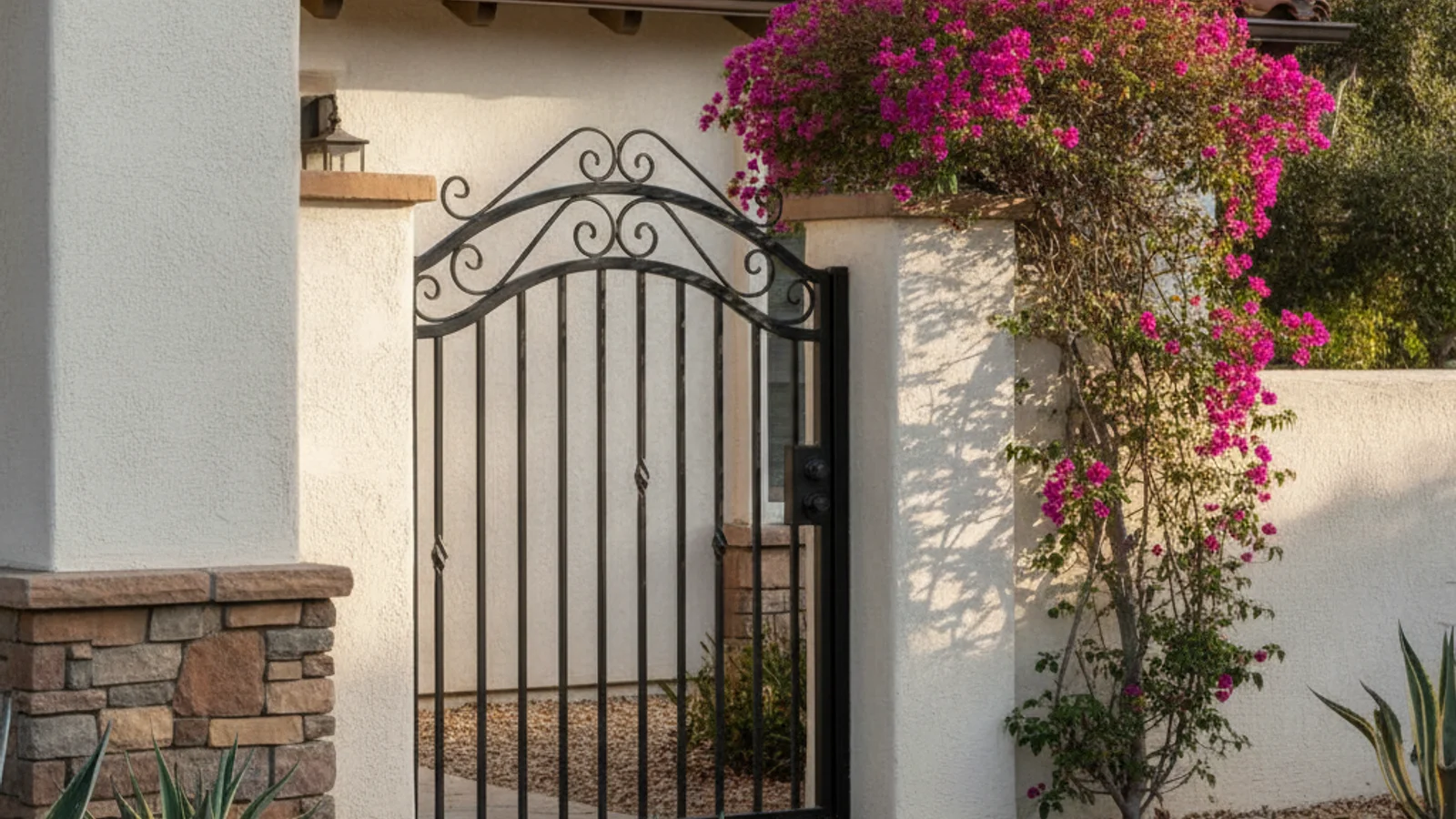 Custom black ornamental steel walk-through gate with scrollwork set into a stucco pillar on a Spanish-style San Diego home.