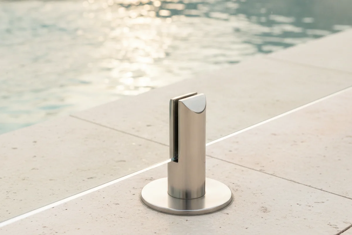Close-up of a 316 stainless steel spigot core-drilled into a pool deck, anchoring a 12mm tempered glass fence panel